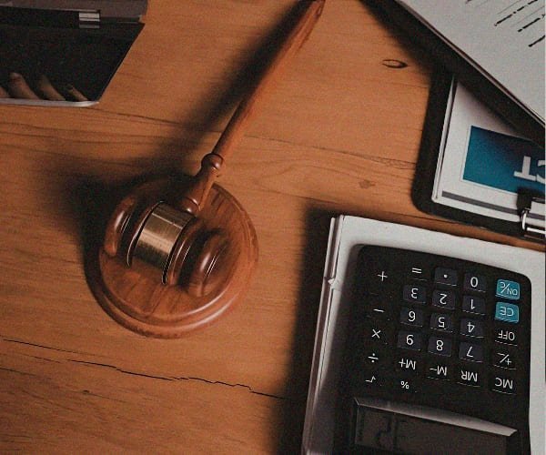 Uma mesa onde aparece um computador, um martelo utilizado em tribunais e uma calculadora.